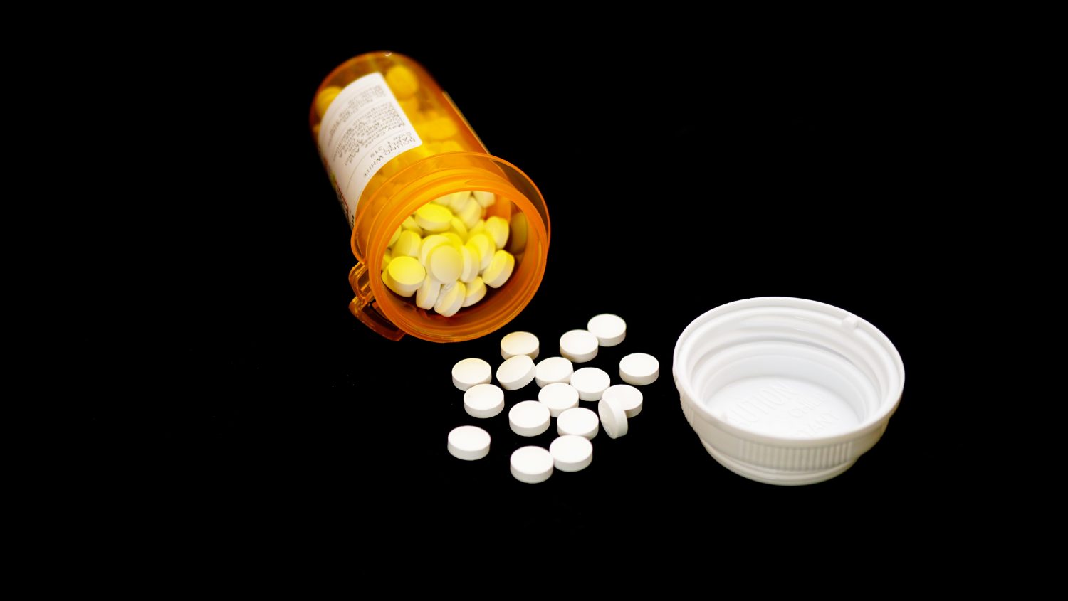 opioid pain pills spilling out of full prescription bottle