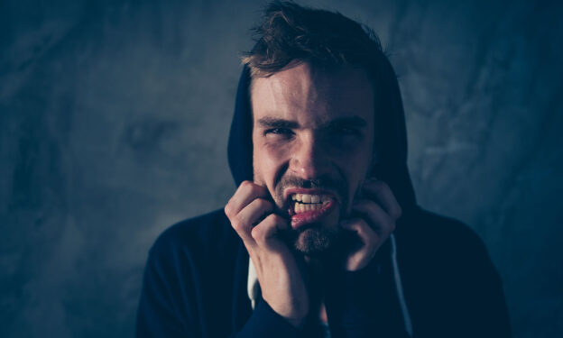 A close-up of a young man, grinning in pain from opiate withdrawals