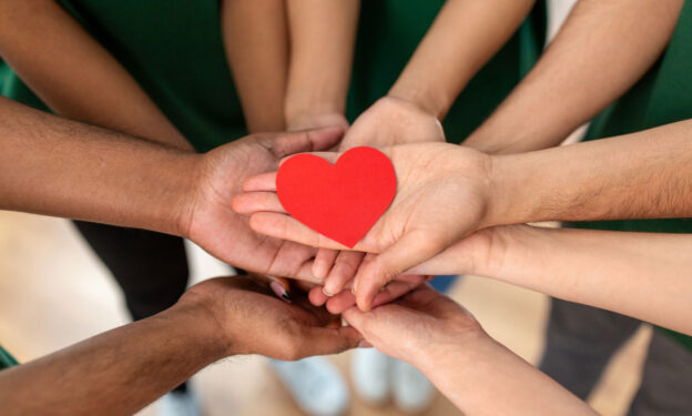 Concept of Overdose vs Suicide: Photo of many adult hands holding a paper cutout of a heart