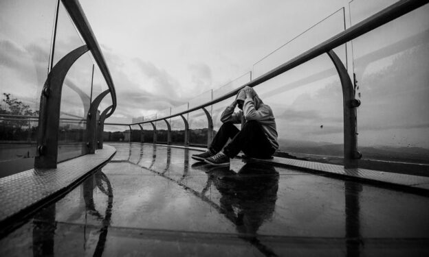 Young depressed man sitting alone in the rain, on a bridge. Concept of fentanyl crisis.
